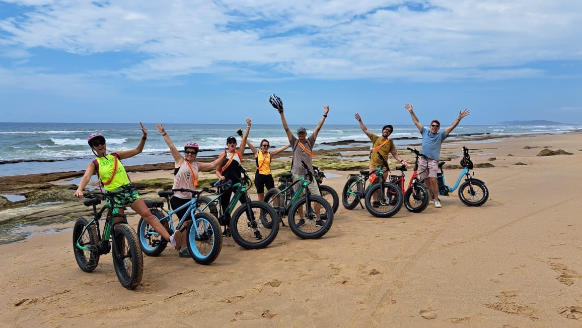 A guided electric fat-bike group celebrating on the beach