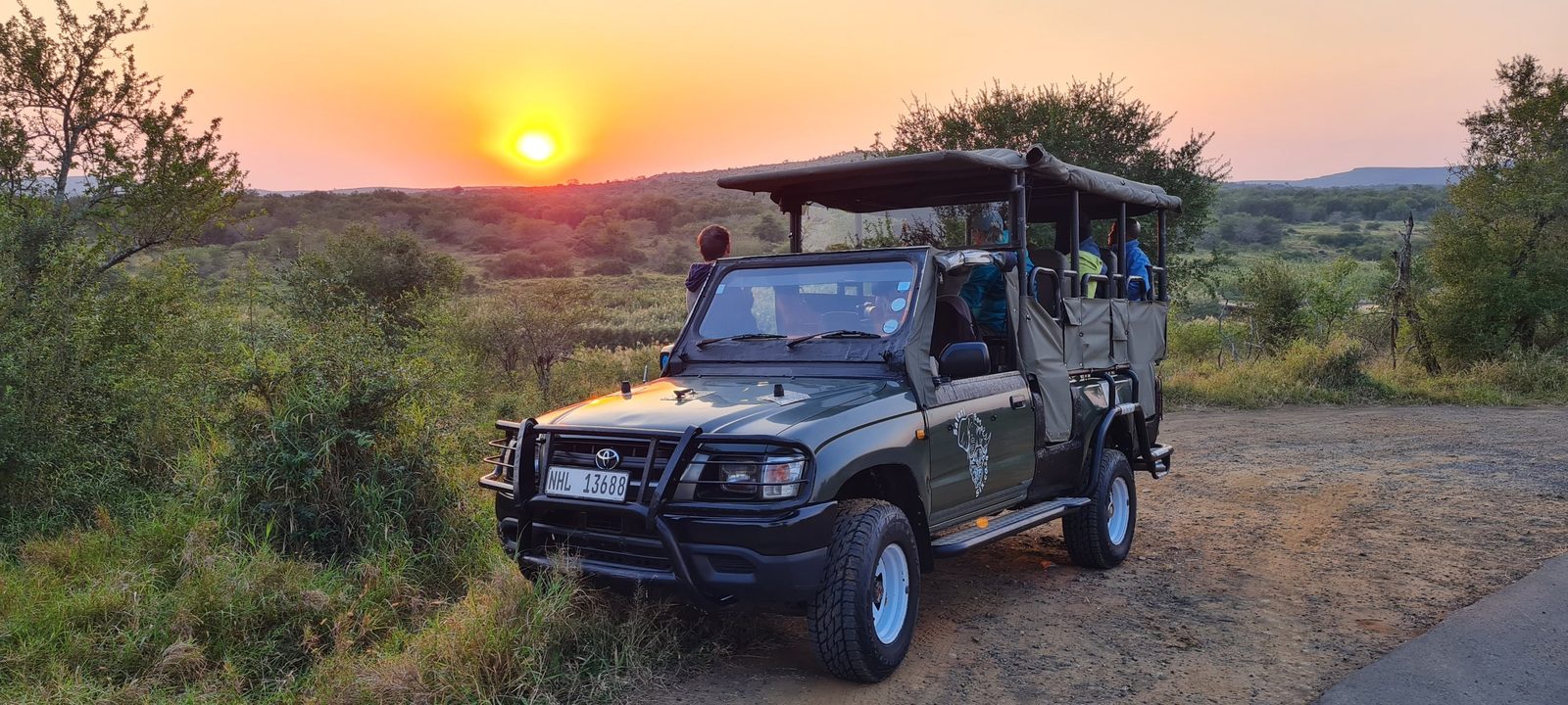 An open game-drive vehicle parked against a bushveld sunset