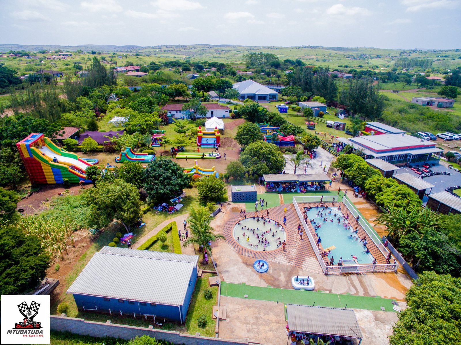Aerial view of a leisure park with swimming pools and lawns, with the town and hills beyond